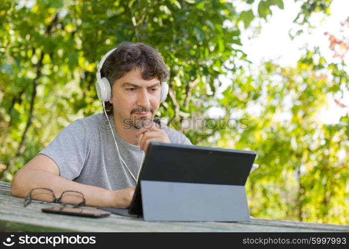 young man working with a tablet pc with headphones, outdoor