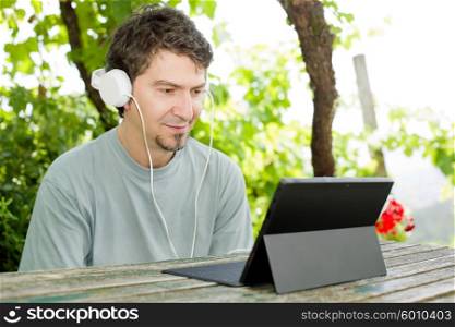 young man working with a tablet pc with headphones, outdoor