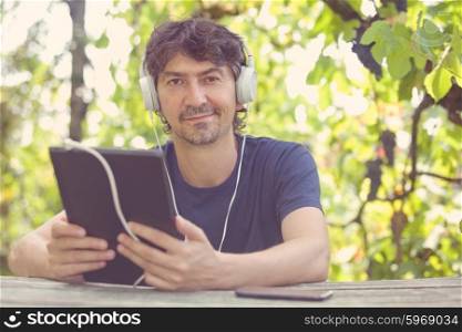 young man working with a tablet pc with headphones, outdoor, filtered image