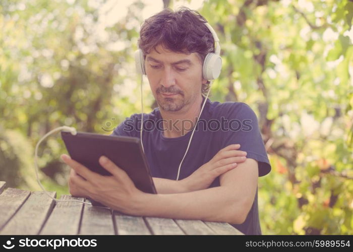 young man working with a tablet pc with headphones, outdoor, filtered image