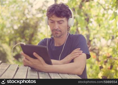 young man working with a tablet pc with headphones, outdoor, filtered image