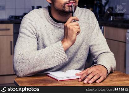 Young man writing at table in kitchen