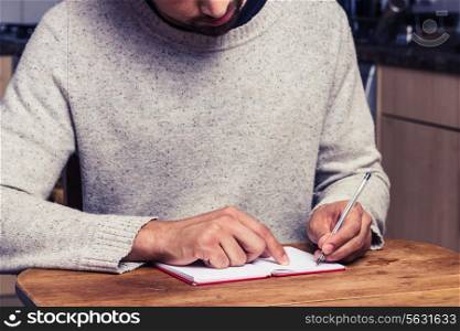 Young man writing in kitchen