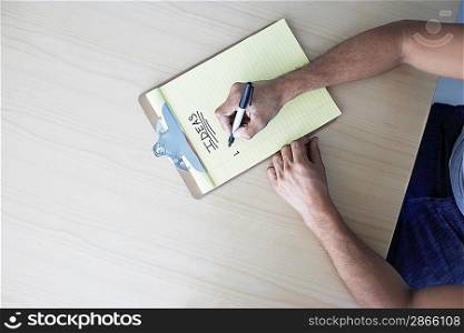 Young man writing on clipboard view from above