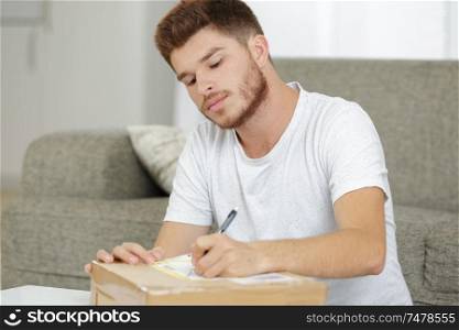 young man writing postage label for parcel