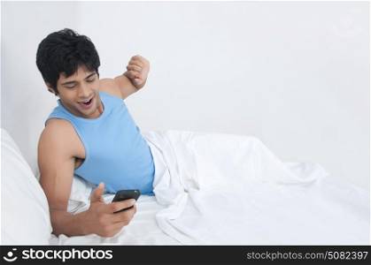 Young man yawning while looking at mobile phone