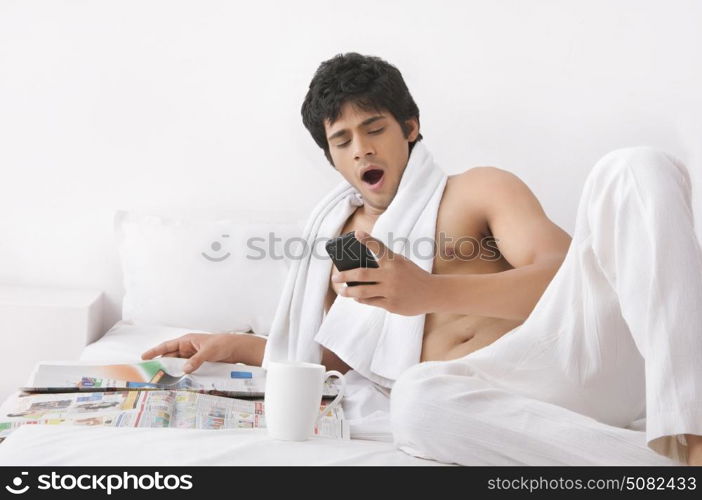 Young man yawning while looking at mobile phone