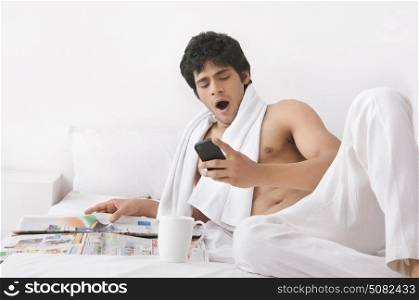 Young man yawning while looking at mobile phone