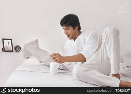 Young man yawning while reading newspaper