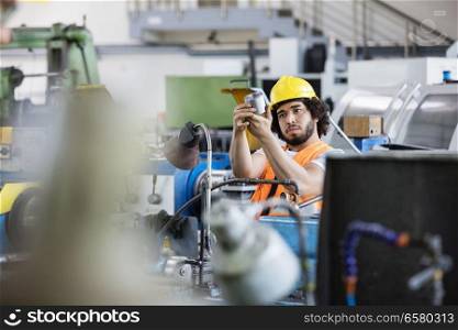 Young manual worker examining metal in factory