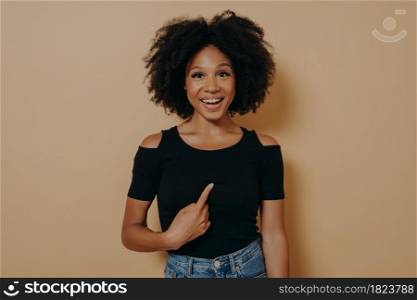 Young mean me? Portrait of happy young mixed race woman pointing finger at herself and looking at camera with amazed face expression, dressed in black t shirt. Body language and human emotions. Overjoyed young mixed race woman pointing finger at herself and looking at camera with amazed face expression