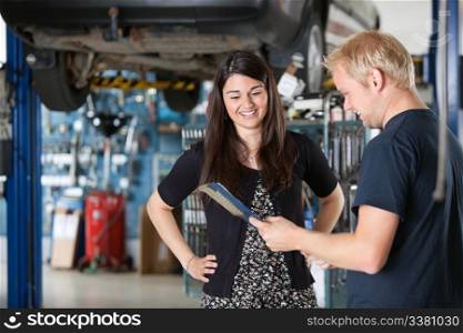 Young mechanic and woman looking at notepad and smiling in garage