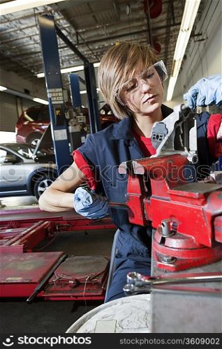Young mechanic in protective clothing concentrating on repairing machine part in garage