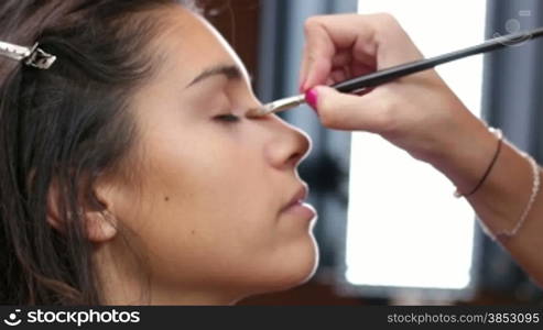 Young Mediterranean girl applying make up.Beautiful woman putting cosmetics.Gorgeous fashion and beauty care close up.Cosmetician making a beauty treatment to an elegance young girl closeups.