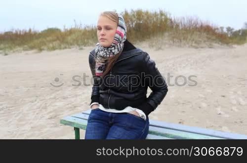 Young melancholy girl is sitting on a bench near the sea.
