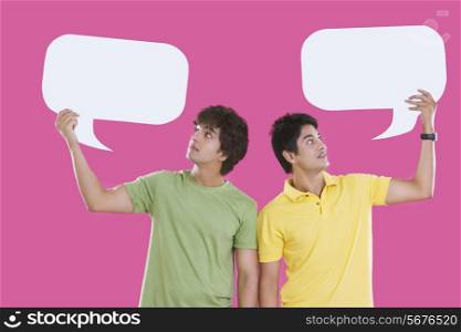 Young men holding speech bubbles isolated over pink background