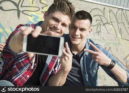 Young men in skatepark, taking self portrait photograph, using smartphone