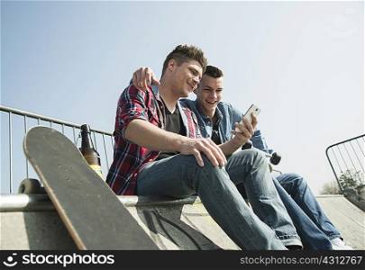 Young men in skatepark, using smartphone, drinking bottle of beer