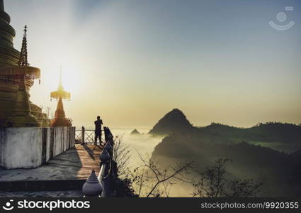 Young men stand to take pictures of the scenery Where fog flows through the gorges The golden light of the sun shines on Wat Phra That Rattana Chedi Tak, Thailand.