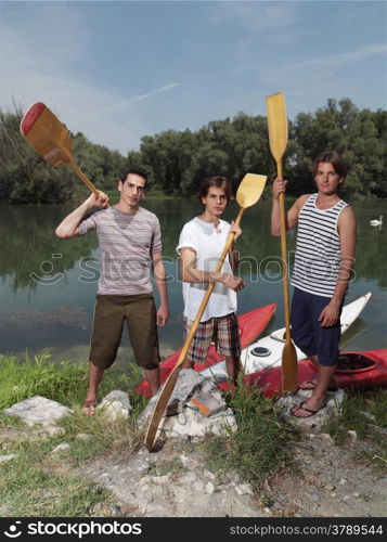 Young men with friends near river, discussing how to paddle in a kayak