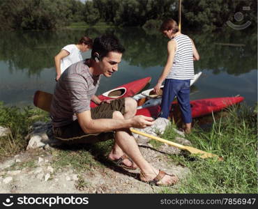 Young men with friends near river, discussing how to paddle in a kayak