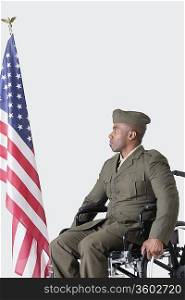 Young military soldier in wheelchair looking at American flag over gray background
