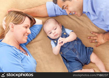 Young Mixed Race Couple Laying With Their Infant On A Blanket.