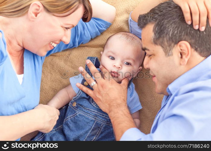 Young Mixed Race Couple Laying With Their Infant On A Blanket.