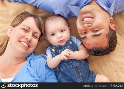 Young Mixed Race Couple Laying With Their Infant On A Blanket.