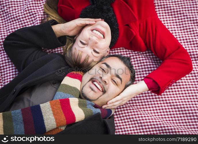 Young Mixed Race Couple Wearing Winter Clothing on Blanket in Park.