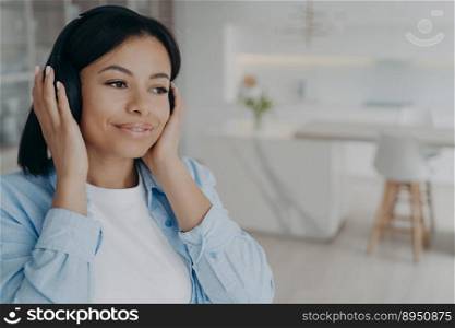 Young mixed race romantic lady is listening to radio in headphones, dreaming and smiling. Happy european girl taking pleasure from music. Enjoying weekend morning at home. Emotions and relaxation.. Young mixed race romantic lady is listening to radio in headphones, dreaming and smiling.