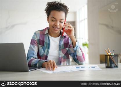Young mixed race teen girl discussing homework with classmate by phone sitting at desk with laptop. Friendly schoolgirl student chatting with friend during exam preparation at home.. Biracial teen girl call by phone, doing homework, sitting at desk with laptop. Education and tech
