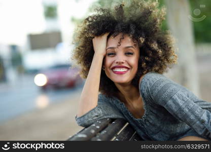 Young mixed woman with afro hairstyle smiling in urban background. Black girl wearing casual clothes.