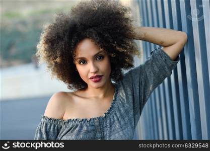 Young mixed woman with afro hairstyle standing in urban background. Black girl wearing casual clothes.