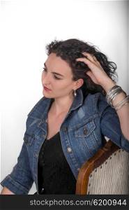 Young model in her mid twenties sitting on a wooden chair with a blue denim jacket.