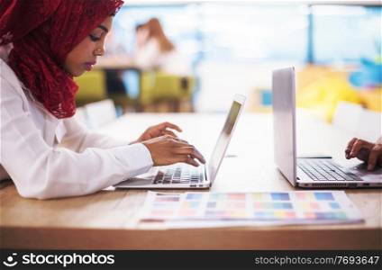 Young modern black muslim business woman wearing a red hijab,working on laptop computer in startup office. Diversity, multiracial concept
