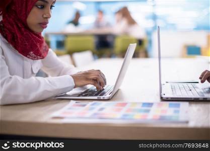 Young modern black muslim business woman wearing a red hijab,working on laptop computer in startup office. Diversity, multiracial concept