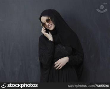 young modern muslim business woman using smartphone wearing sunglasses and hijab clothes in front of black chalkboard