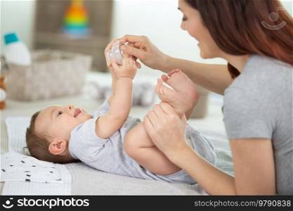 young mom is changing her cute baby diaper cropped