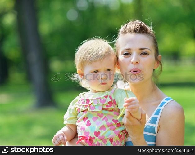 Young mother and baby blowing away dandelion
