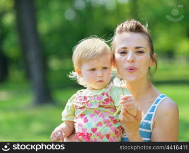 Young mother and baby blowing away dandelion