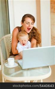 Young mother and baby yawing while working on laptop&#xA;