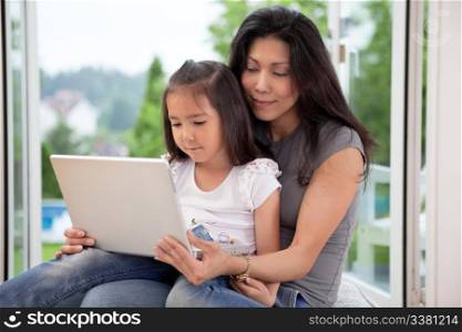 Young mother and daughter at home looking at laptop