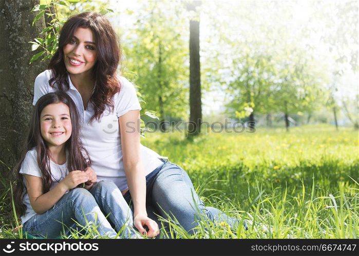Young mother and daughter in park. Beautiful young mother and daughter relaxing sitting on grass in park