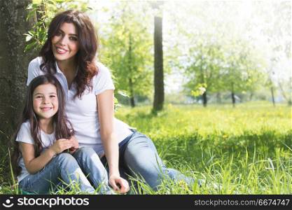 Young mother and daughter in park. Beautiful young mother and daughter relaxing sitting on grass in park