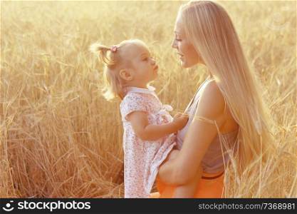 young mother and daughter kissing in the summer in wheat field