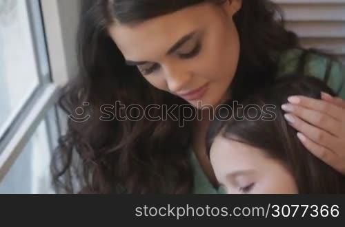 Young mother and daughter look together in window