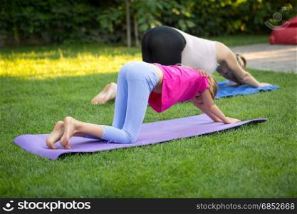 Young mother and daughter practicing yoga on grass
