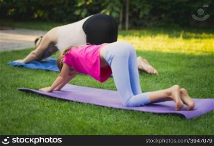 Young mother and daughter practicing yoga on grass at park