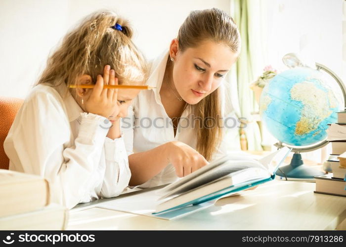 Young mother and daughter reading textbook while doing homework